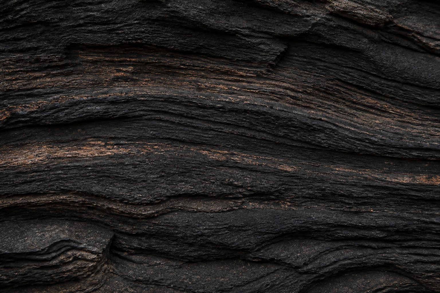 Dark layered rock strata, each band a record of a process that has passed through it