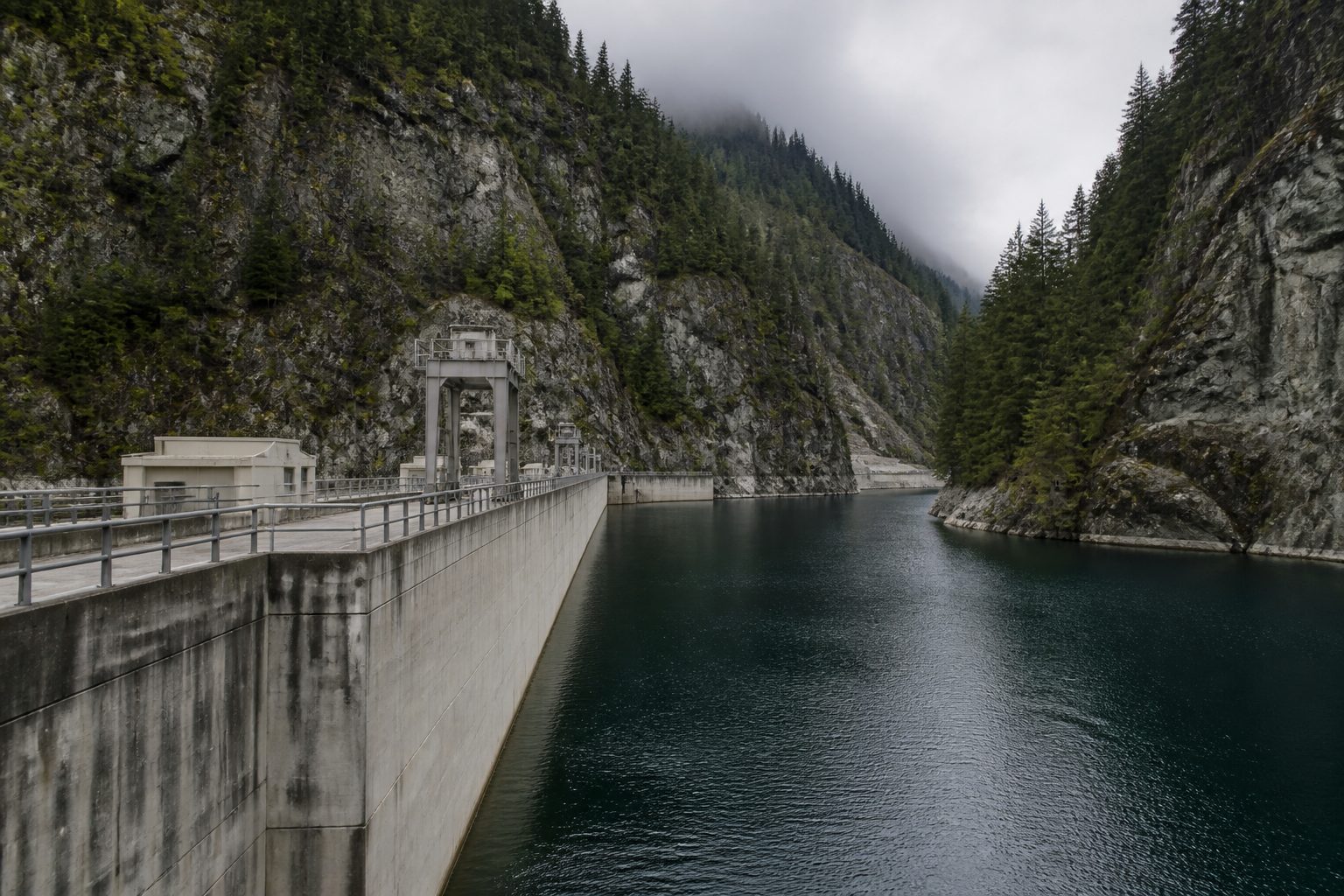 A dam and reservoir set into steep terrain, built infrastructure meeting the landscape it depends on